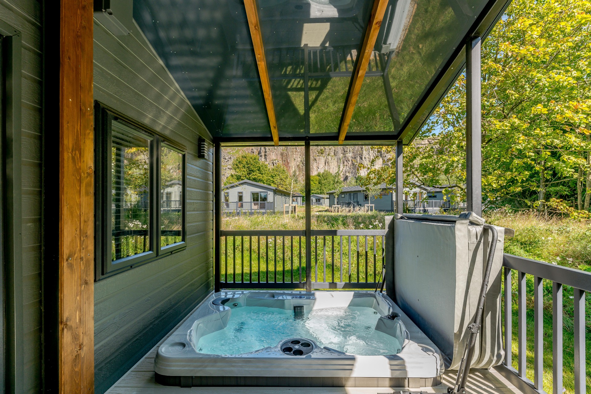 a hot tub is sunken into a veranda. Greenery and lodges are in the background