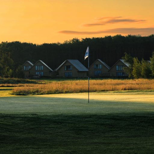 Row of lodges with pitched roofs , the sun is rising and there's a light frost in the foreground on the golf course, with flag